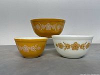 Front on view of three Pyrex nesting bowls, two mustard yellow and one white with floral design.