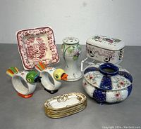 Group photo showing entire lot from a front angle on gray surface against gray background, including ashtrays, trays, figurines, shaker, lidded bowl, and box.
