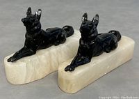 Front angle view of a pair of black metal German Shepherd dog bookends mounted on white stone bases showing detail and condition.
