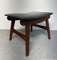 Side view of the wooden frame and black leather top of the ottoman. Shows wear and a small rip on the leather.