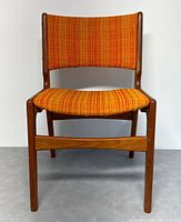 Front view of the teak chair showing orange upholstered seat and back, wood frame, and legs.