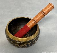 Side view of the singing bowl with wooden striker seated inside it, showing the full size and design details.