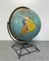 Side view of the vintage globe showing the Americas and metal stand with ring meridian and wire frame base.