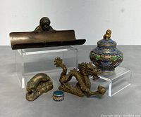 Full view of all items in the lot arranged on display stands, highlighting the brass monkey pen holder, dragon figurine, animal figurine, cloisonne mini jar, and cloisonne ring.
