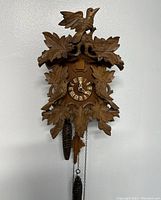 Front view of the carved wooden cuckoo clock hanging on a wall. Shows overall design with leaf and bird carvings.