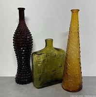 Front view of three vintage glass bottles showing different shapes and colors: yellow-green rectangular, amber conical, and purple elongated diamond textured bottle.
