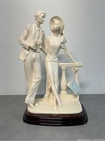 Front view of the vintage Santini porcelain couple sculpture with a man and woman standing on a textured base with a small column, mounted on a dark wooden base.
