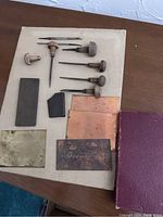 Overview of all antique coffin engraving tools laid out on a table including engraving punches, metal plates, sharpening stone, and other tools.