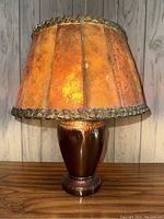 Front view of antique copper lamp with amber mica shade on wood surface.