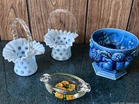 Photo showing the two opalescent dot pattern glass baskets with ruffled edges and clear handles, one cracked, next to a deep blue Inarco Mood Indigo vase with an octagonal base, and a clear glass paperweight trinket dish with orange flowers inside.