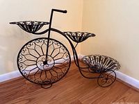 Front angled view of the black metal bicycle plant stand showing all three pot holders and decorative wheel detail.