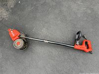Full view of the lawn edger on pavement showing the long handle, motor housing, wheels, and red handle grip