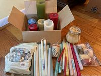 Mixed lot of various candles in an open box and laid out on floor