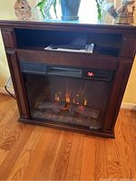 Front view of electric fireplace showing wood mantel, realistic flame effect, faux logs, thermostat display reading 72°F, placed on wooden floor.