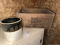 Full view of 2 gallon farmhouse crock next to vintage wood crate marked with embalming fluid text