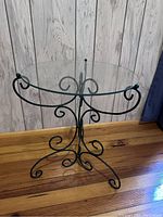 Full view of glass and metal plant stand with decorative scrolled metal legs and support, showing round glass tabletop and overall design.