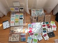 Full assortment of rubber stamps, ink pads, scrapbooking and card making materials arranged on floor in sunlight.