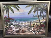 Front view of large framed signed painting depicting a beach scene with two white Adirondack chairs, palm trees, and flowers near the ocean.