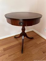 Front view of the round mahogany spider leg table with leather top and drawer closed.