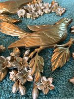 Close-up of one bird wall hanging showing gold metal finish with detailed feather texture and white flowers