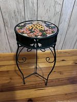 Full view of metal plant stand showing round mosaic tile top with floral and geometric pattern.