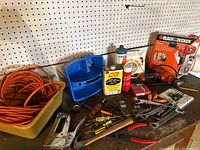 Full view of the tools lined up on pegboard workbench showing a Black & Decker drill in box, extension cord, staple gun, various hand tools, and lubricant cans.