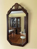 Front view of the mirror showing the carved medallion and frame details reflecting a dining room.