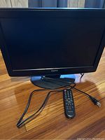 Front view of black Sanyo 19-inch LCD television with screen off, remote control and power cord placed in front on wooden floor.