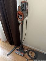 Full view of Shark Rocket vacuum standing upright, showing power cord coiled on floor and vacuum base with brush head.