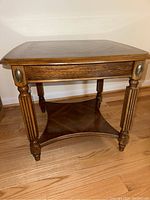 Front angled view of solid wood end table showing bookmatch grain top and turned legs with decorative oval accents