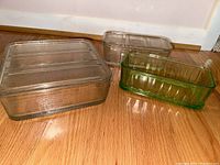 Three glass storage containers, two clear with lids and one green without lid shown on wood floor.
