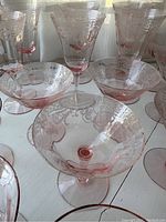 Close-up of 4 pink depression glass coupe stemware glasses showing delicate pressed floral designs, set against window light.