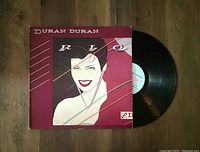 Front cover jacket of Duran Duran's Rio vinyl LP. Shows illustrated woman artwork in maroon and pink tones, with some corner wear on the jacket. The vinyl record partially visible beside jacket appears clean.