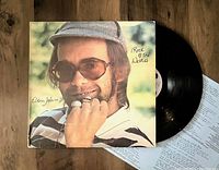 Vinyl record LP with a jacket showing a close-up image of Elton John and the vinyl partially visible with insert underneath.