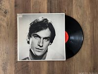 Black vinyl LP partially removed from its original album jacket. Jacket front displays black and white close-up portrait of James Taylor. Red label on vinyl visible.
