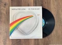 Vinyl LP with original 'In The Heart' album jacket by Kool & The Gang, showing front cover artwork with heart plate and rainbow design alongside black vinyl disc.