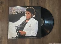 Photo showing Michael Jackson Thriller vinyl LP record and jacket, 1982 1st pressing, jacket and vinyl in very good condition.