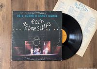 Neil Young & Crazy Horse Rust Never Sleeps vinyl record partially pulled out with visible album jacket and insert behind it on wooden surface