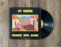 Photo of Ry Cooder Chicken Skin Music vinyl record partially pulled out from illustrated sleeve showing colorful Mexican village artwork and skeleton figure on front cover.