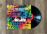 Photo of The Monkees Instant Replay vinyl LP with colorful mosaic album cover and visible black vinyl record with red label.