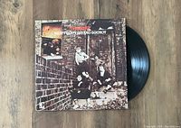 Photo showing The Who 'Meaty, Beaty, Big & Bouncy' vinyl record LP partially out of its album cover placed on wood surface.