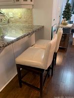 Side view of two beige bar stools positioned next to kitchen counter, showing seat and base details