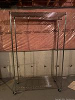 Front view of large metal clothing rack with shelves and caster wheels