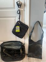 The image shows a black leather crossbody satchel purse (worn) and a large black Olivia and Joy handbag. The satchel purse has a textured finish and some wear signs. The handbag is large with a smooth finish and features an external zippered pocket.