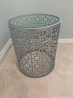 Full view of the round accent table showing the metal geometric patterned base and glass top.