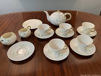 Five cups on saucers, one extra saucer, teapot, creamer, sugar bowl, salad plate arranged on table