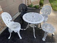 Group shot of three chairs, round table, and side table arranged outside garage