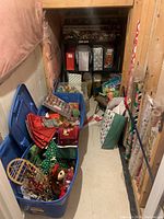 Wide angle image showing aisle with multiple bins filled with Christmas decorations, wrapping paper rolls stored vertically along wall, and gift bags on floor.