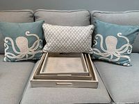 Two blue decorative square pillows with cream octopus design, smaller rectangular pillow with diamond pattern, and three whitewash nested trays on a couch