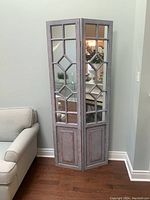 Front view of the two-panel decorative room divider positioned near a couch with mirrors and distressed paint.